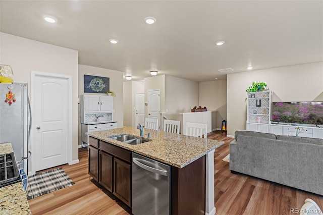 kitchen with light wood finished floors, stainless steel appliances, open floor plan, dark brown cabinetry, and a sink