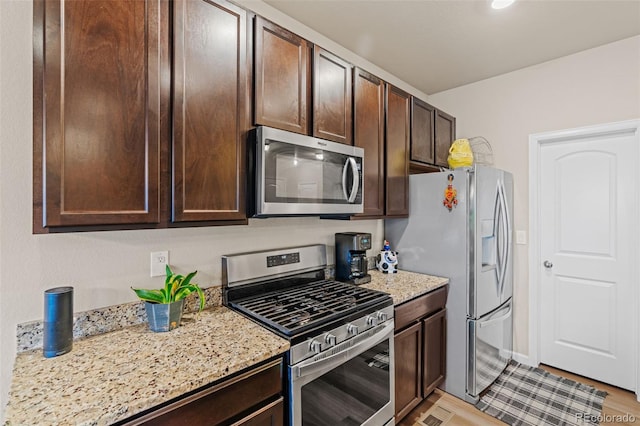 kitchen featuring stainless steel appliances, dark brown cabinets, and light stone countertops