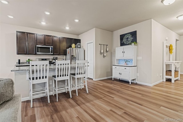 kitchen featuring a breakfast bar area, light wood-style flooring, dark brown cabinetry, baseboards, and appliances with stainless steel finishes