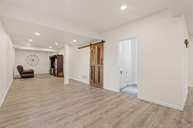 interior space featuring light wood finished floors, a barn door, visible vents, and recessed lighting