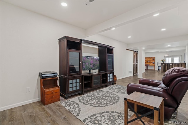 living room featuring a barn door, beamed ceiling, wood finished floors, and baseboards