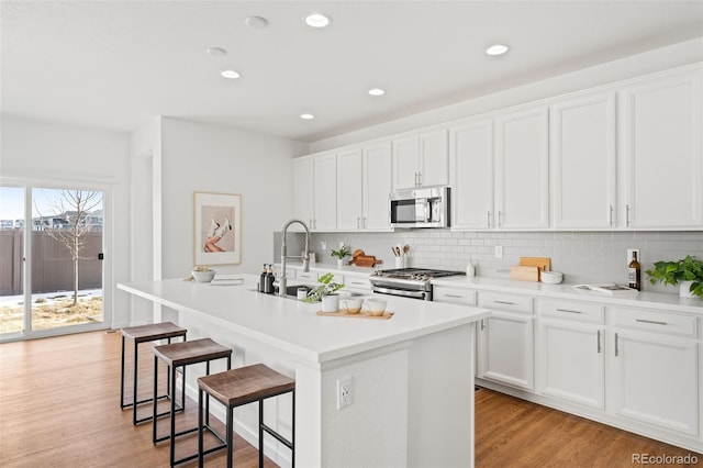 kitchen with a breakfast bar area, white cabinetry, a center island with sink, appliances with stainless steel finishes, and light hardwood / wood-style floors