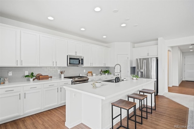 kitchen featuring a kitchen bar, sink, appliances with stainless steel finishes, an island with sink, and white cabinets