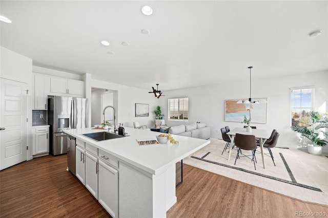 kitchen featuring pendant lighting, white cabinetry, an island with sink, sink, and decorative backsplash