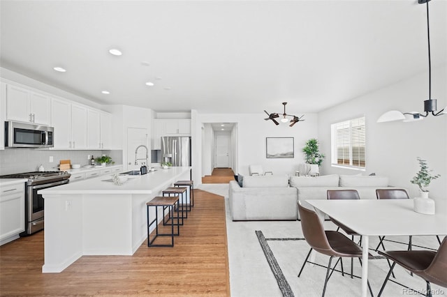 kitchen featuring decorative light fixtures, a breakfast bar area, white cabinets, stainless steel appliances, and a center island with sink