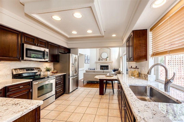 kitchen featuring dark brown cabinetry, a tray ceiling, a sink, appliances with stainless steel finishes, and light tile patterned floors