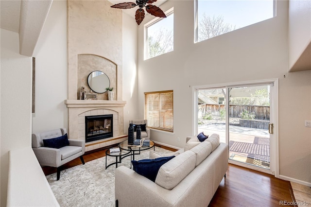 living room with ceiling fan, a tiled fireplace, a healthy amount of sunlight, and wood finished floors