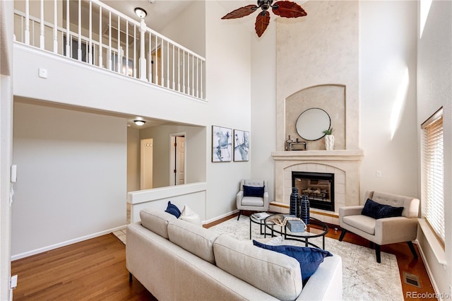 living room with visible vents, wood finished floors, a high ceiling, a tiled fireplace, and a ceiling fan