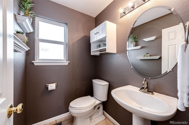 bathroom featuring toilet, baseboards, a sink, and tile patterned floors