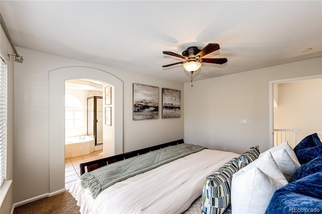 carpeted bedroom featuring arched walkways, a ceiling fan, and ensuite bath