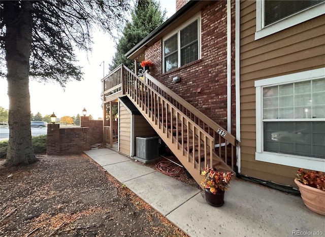 view of property exterior with central AC, stairway, brick siding, and a chimney