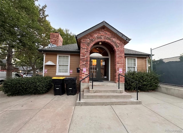 view of exterior entry featuring french doors, a chimney, roof with shingles, and fence