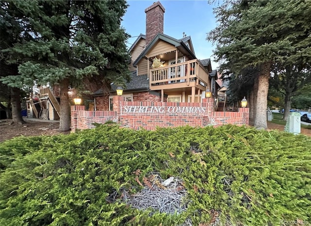 rear view of property with a balcony, a chimney, brick siding, and fence