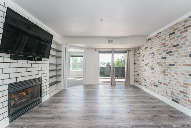 12118 W Dorado Pl Unit 206, Littleton, CO 80127 - unfurnished living room with brick wall, a textured ceiling, a lit fireplace, ornamental molding, and wood finished floors