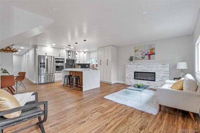 living room featuring sink, a stone fireplace, and light hardwood / wood-style flooring