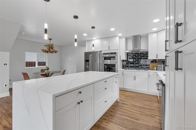 kitchen featuring light wood-style flooring, appliances with stainless steel finishes, wall chimney exhaust hood, tasteful backsplash, and a center island