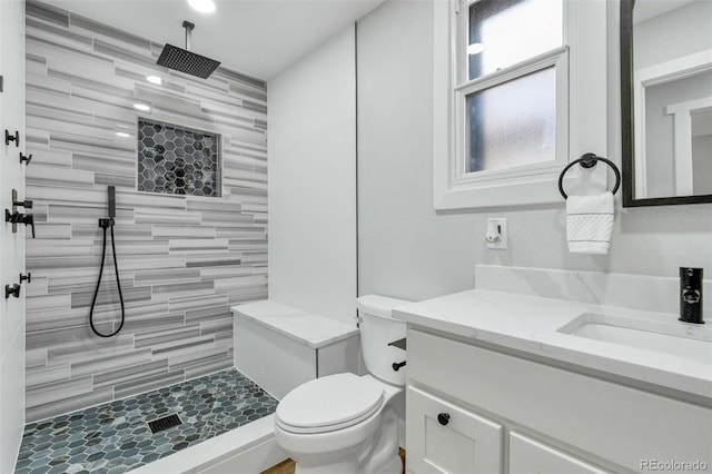 full bathroom with a tile shower, toilet, and vanity