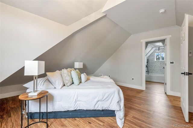 bedroom with vaulted ceiling, wood finished floors, and baseboards