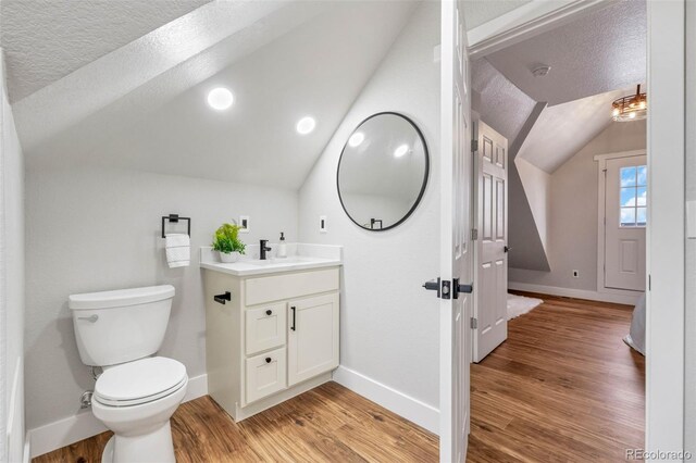 half bathroom featuring toilet, vanity, vaulted ceiling, wood finished floors, and a textured ceiling