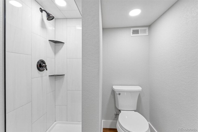 full bathroom with visible vents, baseboards, toilet, a tile shower, and a textured wall