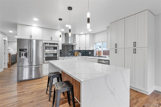 kitchen featuring white cabinetry, wall chimney range hood, light wood-style floors, and stainless steel appliances