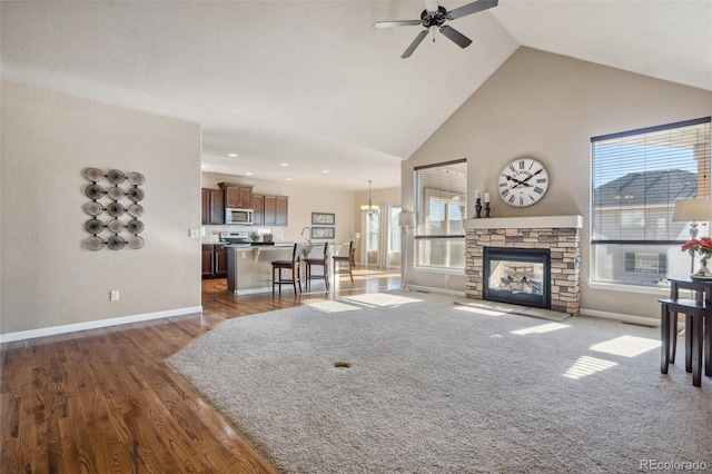 living room with ceiling fan with notable chandelier, a stone fireplace, dark wood-type flooring, and high vaulted ceiling