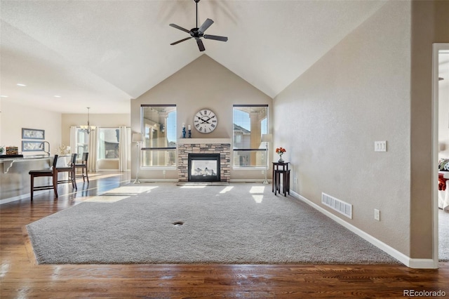 living room with ceiling fan with notable chandelier, dark hardwood / wood-style floors, a stone fireplace, and vaulted ceiling