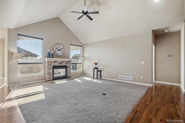 unfurnished living room featuring ceiling fan, dark hardwood / wood-style floors, a stone fireplace, and a wealth of natural light