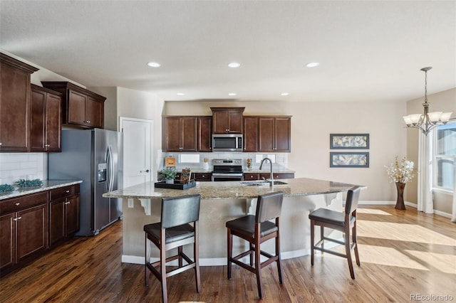 kitchen featuring stainless steel appliances, an inviting chandelier, tasteful backsplash, a kitchen island with sink, and hardwood / wood-style flooring