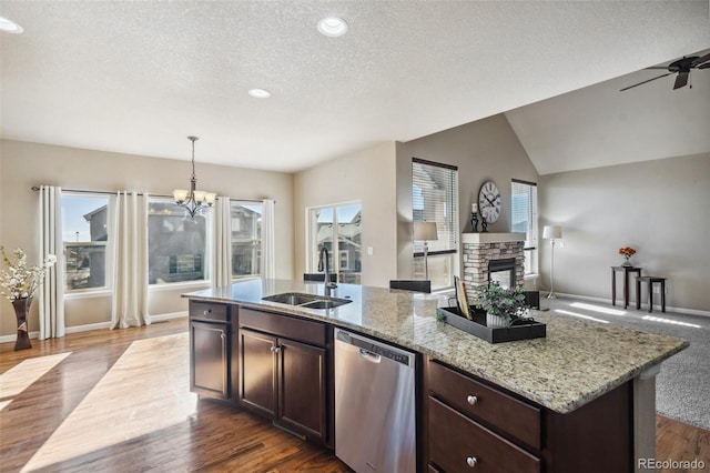 kitchen with stainless steel dishwasher, dark brown cabinets, sink, a stone fireplace, and hanging light fixtures