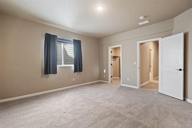 unfurnished bedroom with a textured ceiling, a walk in closet, light carpet, and a closet