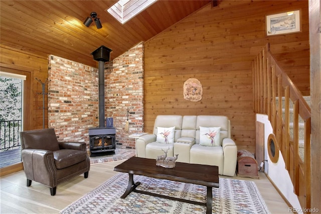 living room featuring wood ceiling, a wood stove, lofted ceiling with skylight, light hardwood / wood-style flooring, and wooden walls