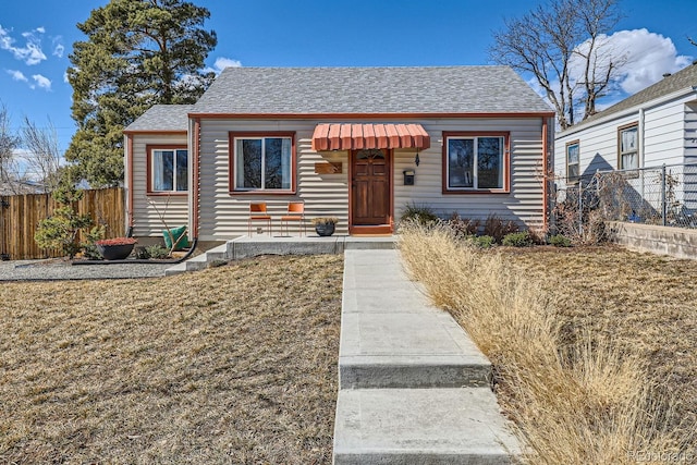 bungalow-style house with a shingled roof, a front yard, and fence