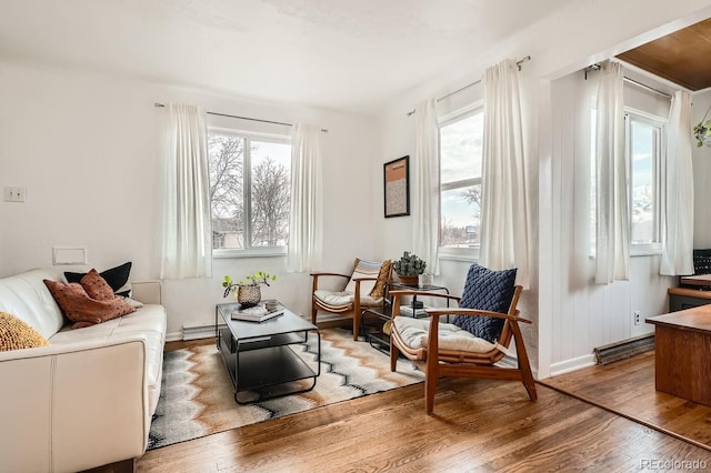 living area with a wealth of natural light, a baseboard radiator, and hardwood / wood-style flooring