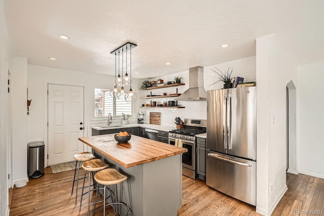 kitchen featuring island exhaust hood, gray cabinets, stainless steel appliances, a kitchen bar, and open shelves