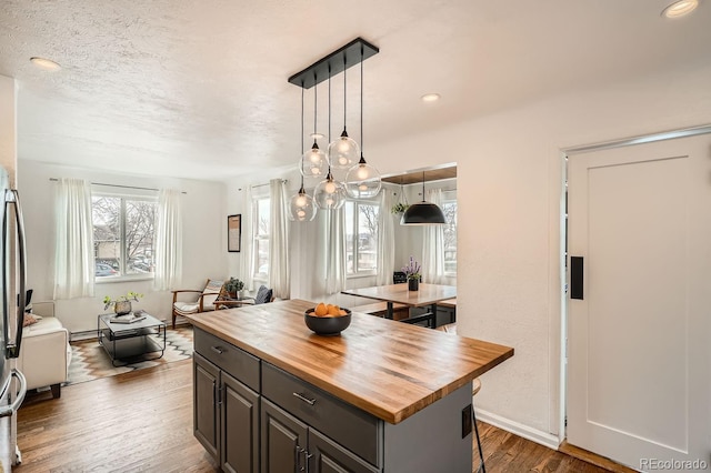 kitchen featuring butcher block countertops, wood finished floors, a center island, hanging light fixtures, and a kitchen bar