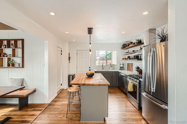 kitchen with gray cabinetry, stainless steel appliances, a breakfast bar, hanging light fixtures, and open shelves