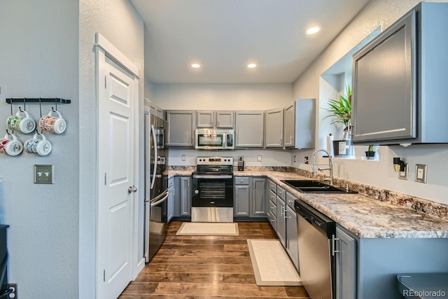 kitchen with gray cabinetry, sink, stainless steel appliances, light stone counters, and dark hardwood / wood-style floors