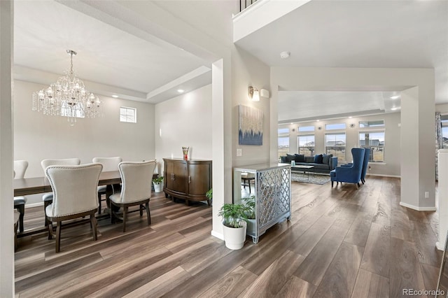 dining area featuring a raised ceiling, a notable chandelier, and dark hardwood / wood-style flooring