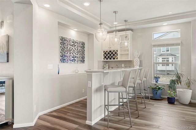 bar featuring pendant lighting, white cabinetry, a tray ceiling, wood-type flooring, and decorative backsplash