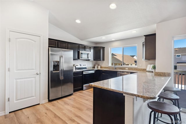 kitchen with lofted ceiling, a breakfast bar area, kitchen peninsula, stainless steel appliances, and light hardwood / wood-style flooring