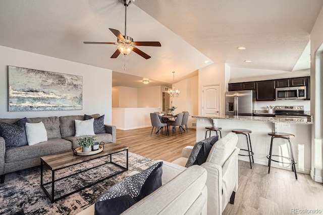 living room with vaulted ceiling, ceiling fan with notable chandelier, and light hardwood / wood-style floors