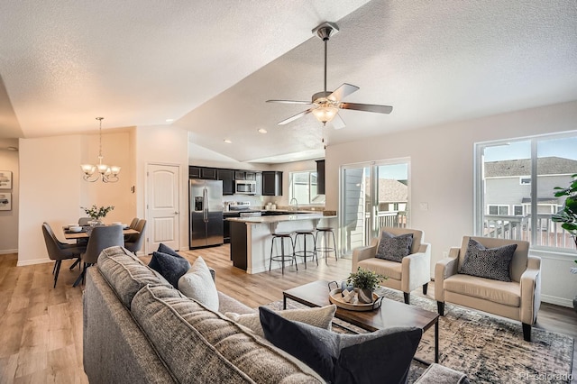 living room featuring ceiling fan with notable chandelier, lofted ceiling, sink, a textured ceiling, and light hardwood / wood-style flooring