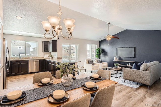 dining space with ceiling fan with notable chandelier, lofted ceiling, sink, a textured ceiling, and light hardwood / wood-style flooring