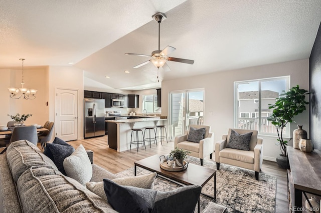 living room with lofted ceiling, ceiling fan with notable chandelier, light hardwood / wood-style floors, and a textured ceiling