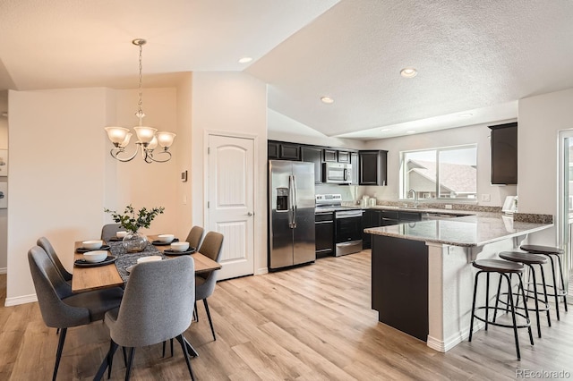 kitchen with decorative light fixtures, appliances with stainless steel finishes, kitchen peninsula, light stone countertops, and light hardwood / wood-style floors