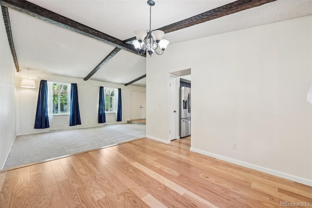 empty room with a textured ceiling, beamed ceiling, light wood-type flooring, and a chandelier