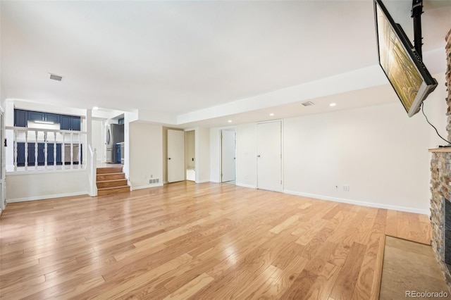 unfurnished living room with light wood-type flooring and a stone fireplace