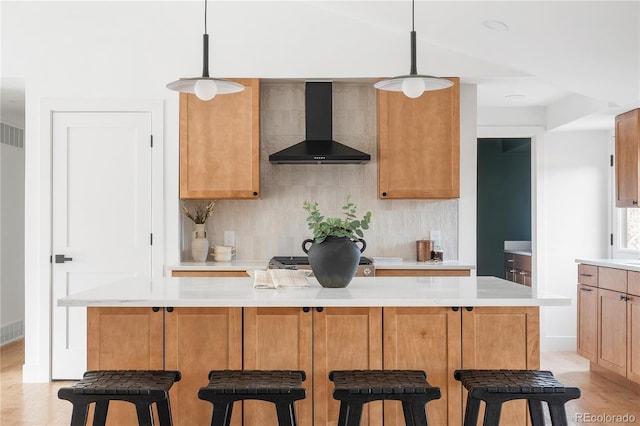 kitchen featuring wall chimney exhaust hood, a kitchen island, a breakfast bar, and hanging light fixtures