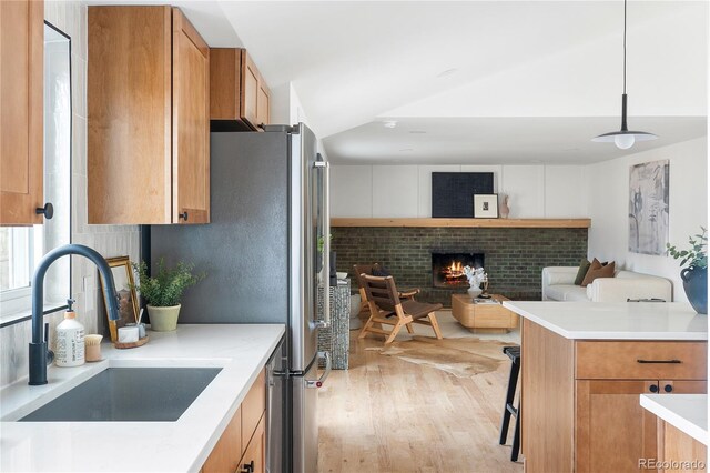 kitchen featuring vaulted ceiling, pendant lighting, sink, a brick fireplace, and light hardwood / wood-style flooring